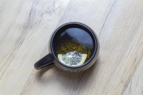 Green tea with lemon in a black cup on a wooden parquet Stock Photos
