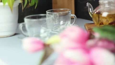 Green tea is poured into a cup from a transparent glass teapot. Dark blurred Stock Footage 152043928