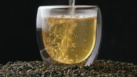 Green tea is poured into a slowly rotating glass, swirling golden infusion among Stock Footage 318650587