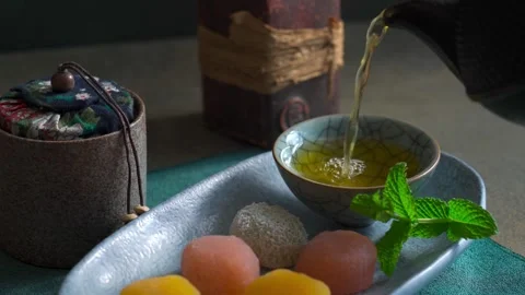 Green tea is pouring into cup alongside traditional Japanese mochi treats Stock Footage 336310860