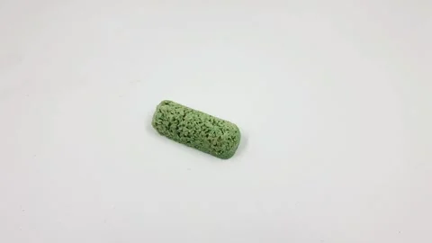 Green textured cylindrical object rolling across white surface motion footage Stock Footage 331791617
