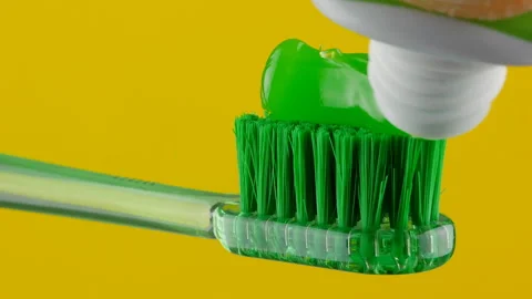 Green toothpaste is placed on a green toothbrush on a yellow background in close Stock Footage 147120452