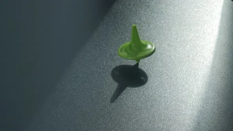 A green top spins on a dark table Stock Footage 132358169