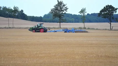 A green tractor with caterpillar tracks pulls a large blue plow across a Stock Footage 313329817