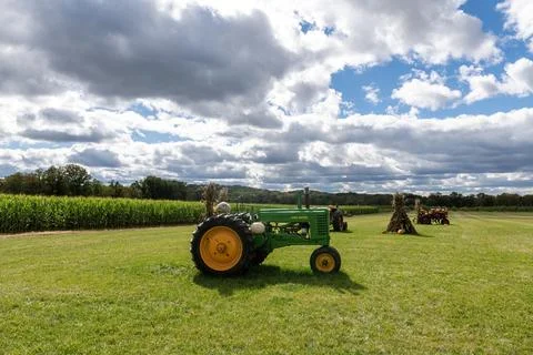 Green Tractor in Field Surrounded by Corn and Clouds on Sunny Afternoon Stock Photos