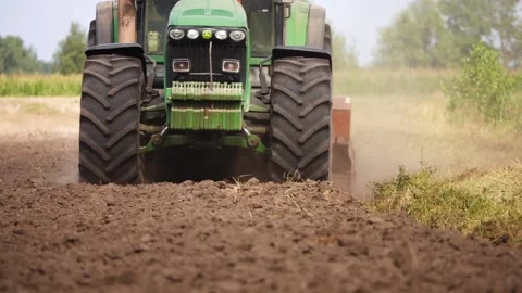 Green tractor with large wheels rides over the field and plow the soil after  Stock Footage 153384799