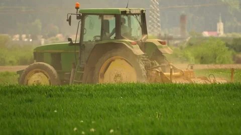 Green tractor plowing cereal field between mountains Stock Footage 242999539