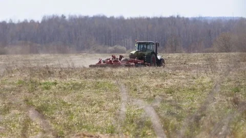 Green tractor plowing large dry field with forest background under clear sk.. Stock Footage 333702119