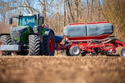Green tractor pulls red air seeder across tilled field in spring Stock Photos