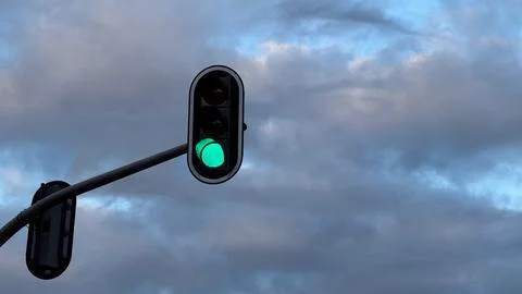 Green traffic light against cloudy sky symbolizing go or forward movement w.. Stock Photos