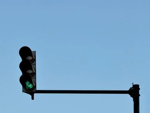 Green traffic light installed on a pole above a roadway, against a blue sky, Foto stock