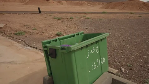 Green trash bin with Arabic text beside desert road in Morocco Stock Footage 337432586