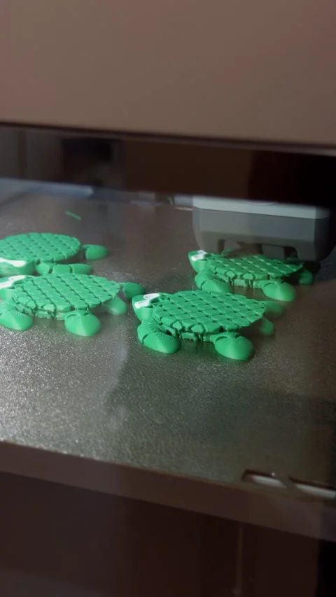 Green turtle figures being printed on 3D printer build plate in close view Stock-Footage 346558157