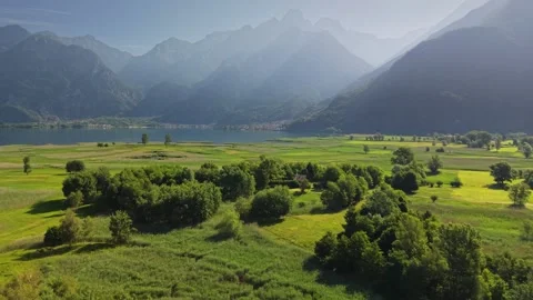 Green valley fields and Lago Mezzola morning scenery under mountain peaks Stock Footage 341755260