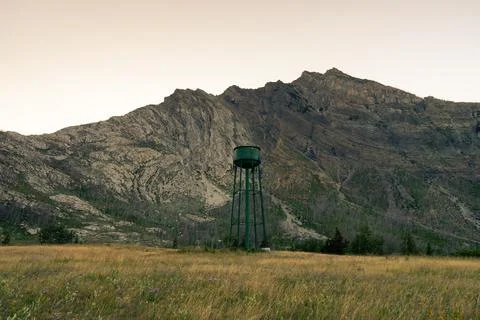 Green water tower stands tall, set against a backdrop of mountains. Stock Photos