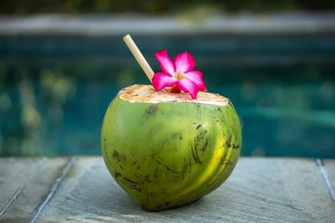 Green young coconut close up with bamboo straw and tropical pink flower on th Stock Photos