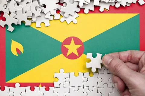 Grenada flag  is depicted on a table on which the human hand folds a puzzle o Foto stock