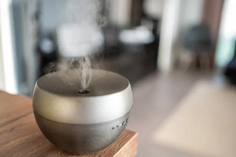 Grey aroma oil diffuser on light table at home, space for text. Air freshener Stock Photos