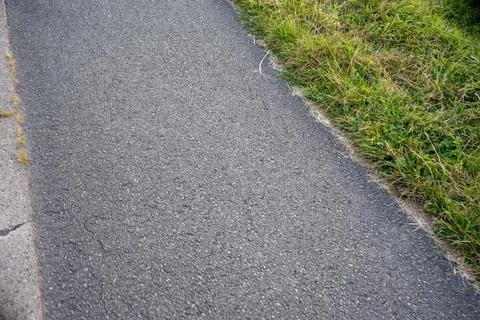 Grey asphalt path with fine grain texture running diagonally beside a strip of Stock Photos