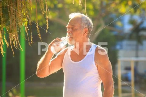 Grey Bearded Old Man in Vest Holds Water Bottle in Park Stock Photos