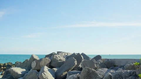 Grey boulder pile and concrete block on shore against blue ocean and clear sky. Stock Footage 346728402
