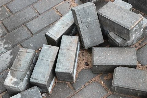 Grey bricks are scattered on a cobblestone pavement, showing the ongoing cons Stock Photos