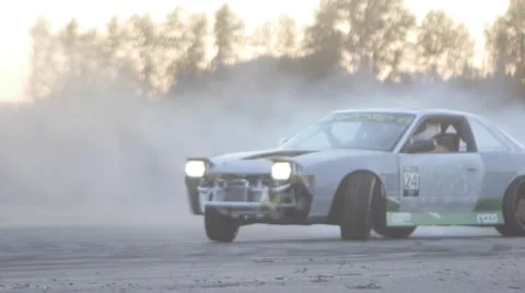 Grey car drifts around corner at dusk leaving behind smoke trail. Stock Footage 59762104