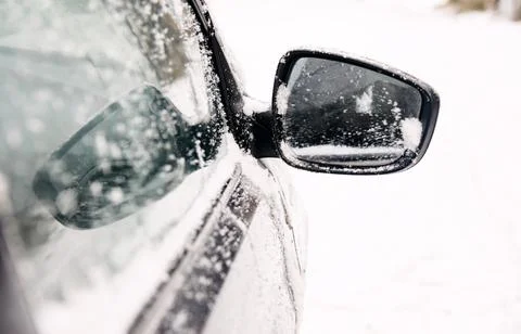 The grey car's cleaned mirror is dusted with snow on the street Stock Photos