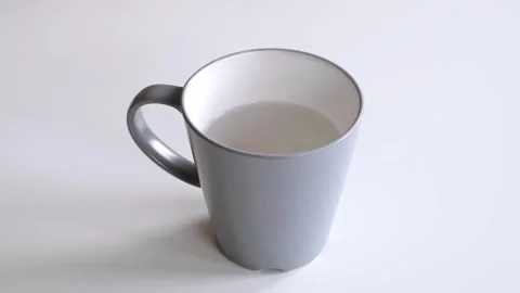 A grey ceramic mug with water stands on a white table, side and top view. Fresh Stock Footage 323501925