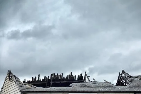 Grey cloudy sky above fire damaged roof with blackened wooden beams and cop.. Stock-Fotos