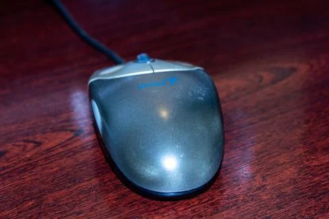 Grey computer mouse on dark brown wooden table surface in office Stock Photos