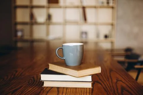 Grey cup on a stack of books on a dark library background, copy space. Stock Photos