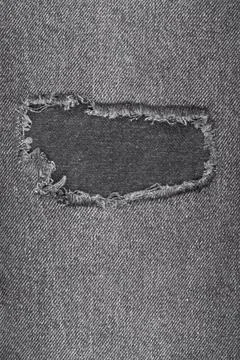 Grey denim fabric texture with rectangular hole. Worn and frayed jean mater.. Stock Photos
