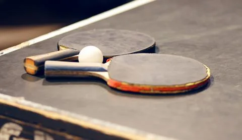 On the grey dusty table are two old battered table tennis rackets and a white Stock Photos