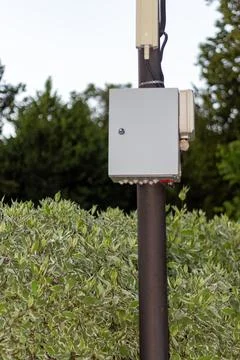 Grey electrical control box mounted on a brown metal pole in nature park Stock Photos