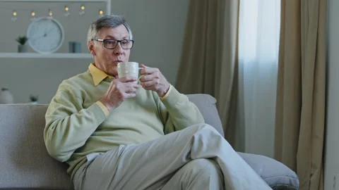 Grey-haired aged man in glasses sitting on couch watching TV enjoying relaxing Video stock 168622258