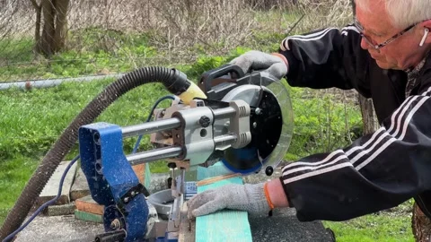 Grey-haired carpenter white man in glasses use large miter saw woodwork on Vídeo Stock 243825192