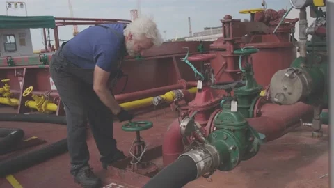 Grey haired donkeyman rotates green valve at pipeline Video stock 148389059