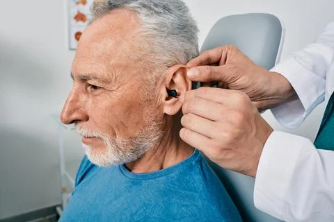 Grey-haired elderly man during installation intra-ear hearing aid into his .. Foto stock