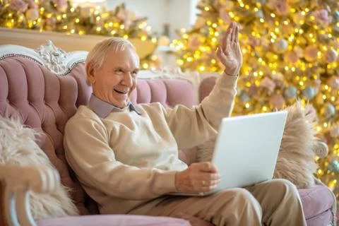 Grey-haired elderly man having a video chat and waving his hand Stock Photos
