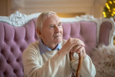 Grey-haired elderly man sitting on the sofa and looking aside Stock Photos