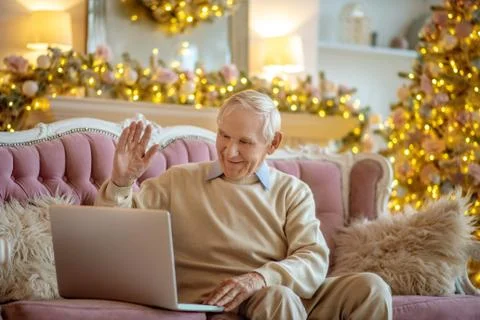 Grey-haired elderly man sitting on the sofa and having a video call Stock-Fotos