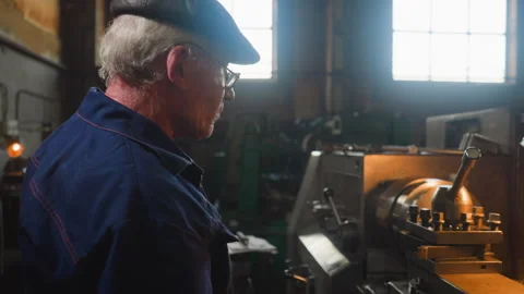 Grey haired employee stands by operating lathe machine Stock Footage 243306955