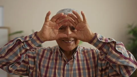 A grey-haired hispanic man in plaid shirt playfully frames his face with ha.. Stock Footage 278282699