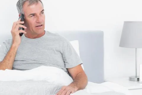 Grey haired man making a phone call in bed Stock Photos