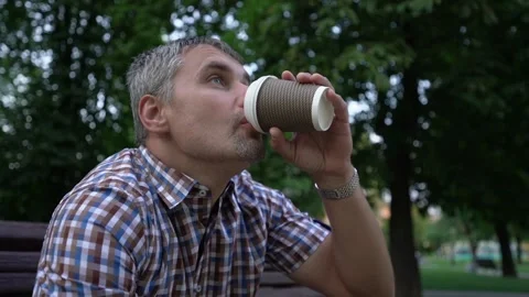 Grey-haired man sips coffee enjoying weather in city park Video stock 167499943