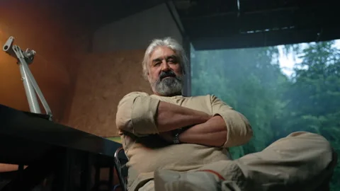 Grey-haired man sits looking satisfied in garage studio Stock Footage 204838370