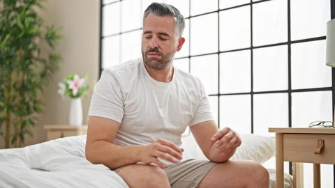 Grey-haired man sitting on bed using smartphone looking upset at bedroom Video stock 246992703