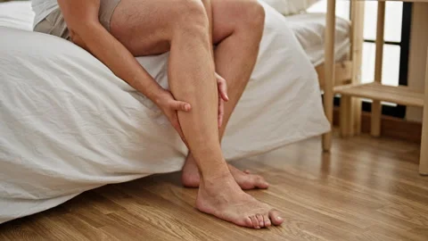 Grey-haired man sitting on bed massaging legs at bedroom Video stock 246992716