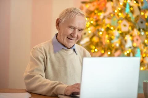 Grey-haired man sitting at the table and working on a laptop Stock Photos